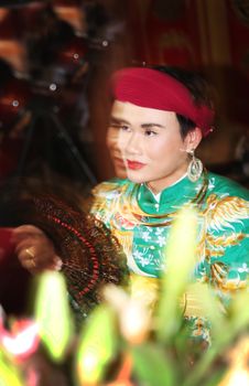 A woman in vibrant traditional clothing holds a fan, blending classic and cultural styles.