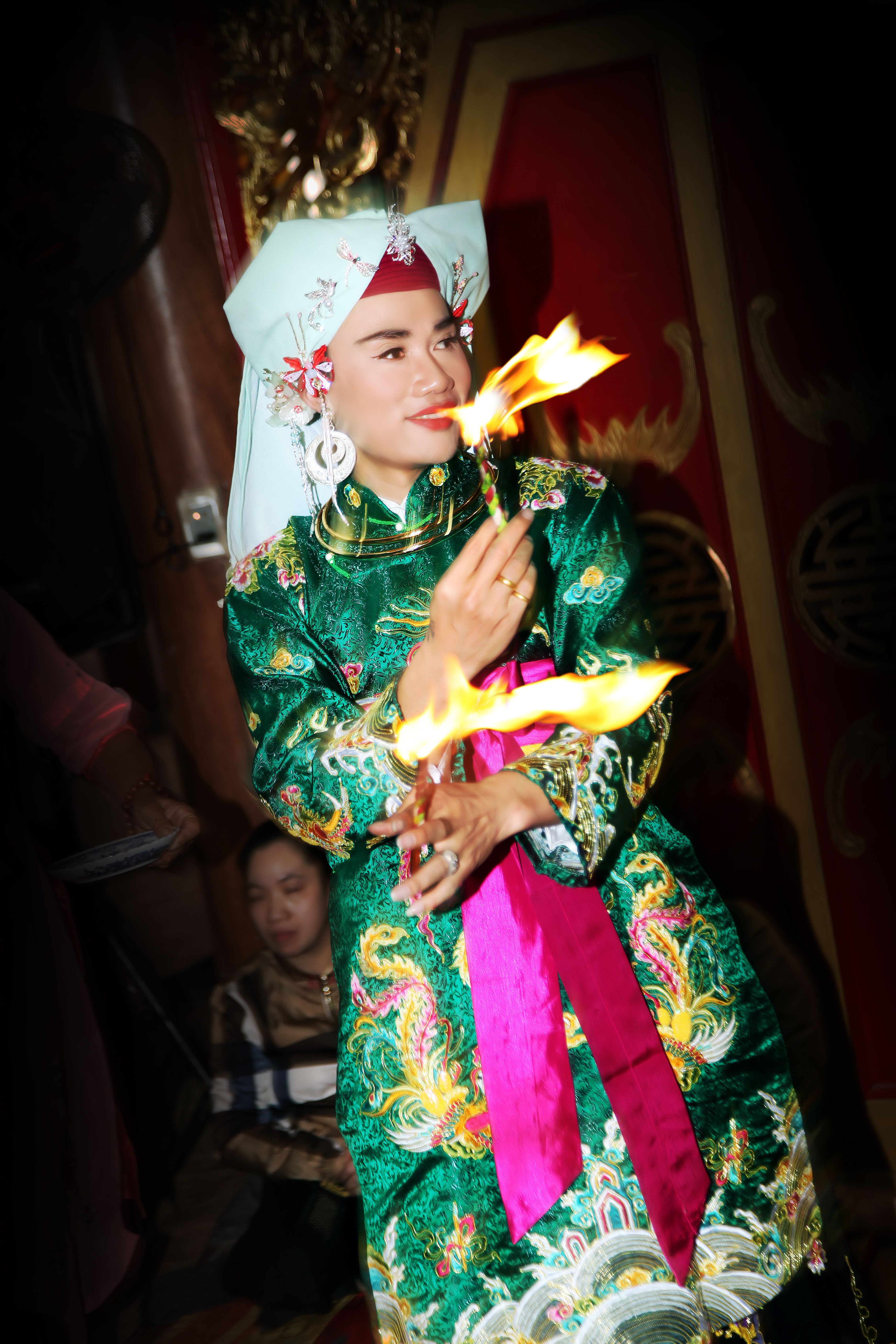 Asian performer in vibrant attire displaying a traditional fire act indoors.