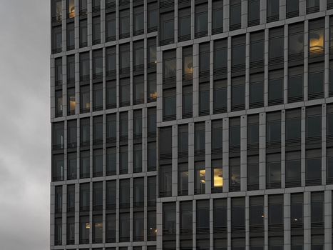 Close-up of a modern office building facade with glowing lights seen through windows at dusk.