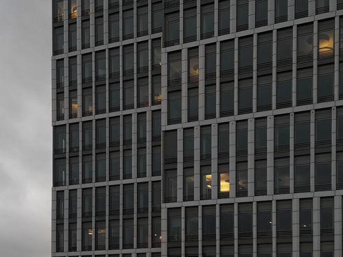 Free Close-up of a modern office building facade with glowing lights seen through windows at dusk. Stock Photo