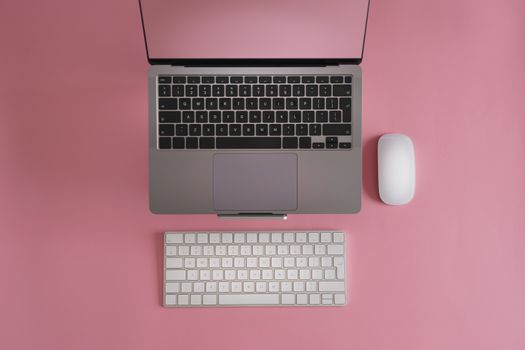 Top view of a laptop, keyboard, and mouse on a pink surface. Perfect for tech-related content.
