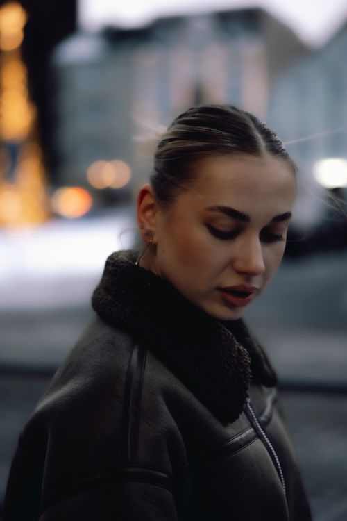 Free Portrait of a woman in a leather jacket outdoors with blurred city lights in the background. Stock Photo