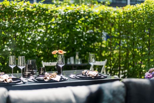 A stylish outdoor dining table set with napkins, wine glasses, and a floral centerpiece against a lush garden backdrop.