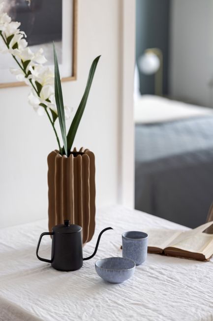 Elegant table setting with teapot, vase, and open book in a cozy indoor environment.