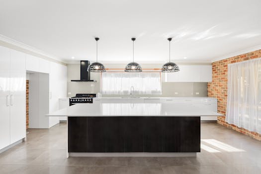 Spacious minimalist kitchen featuring white cabinets, pendant lighting, and brick walls.