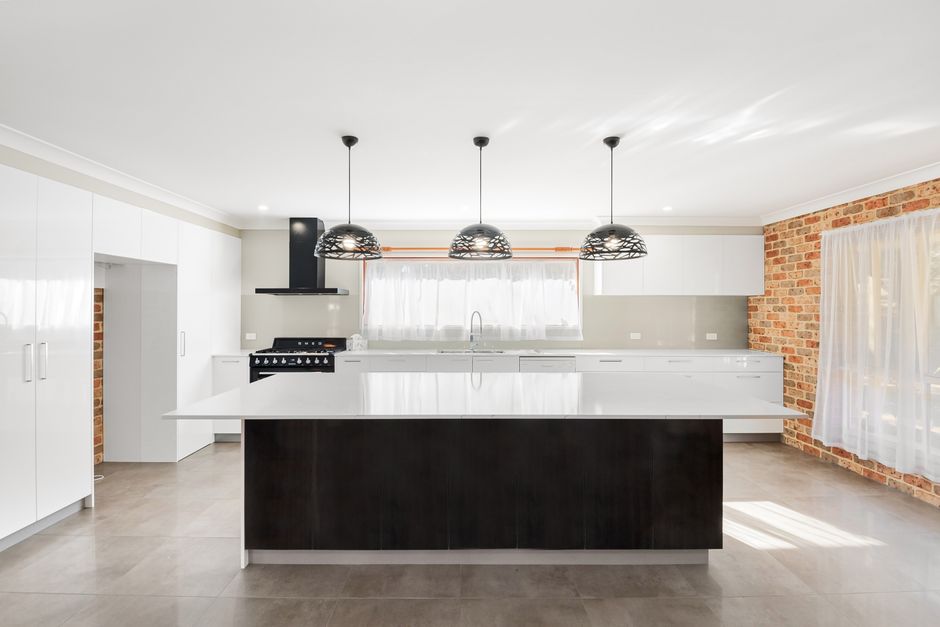 A sleek, modern kitchen in a renovated Sydney home, featuring integrated appliances, stone countertops, and warm timber accents.