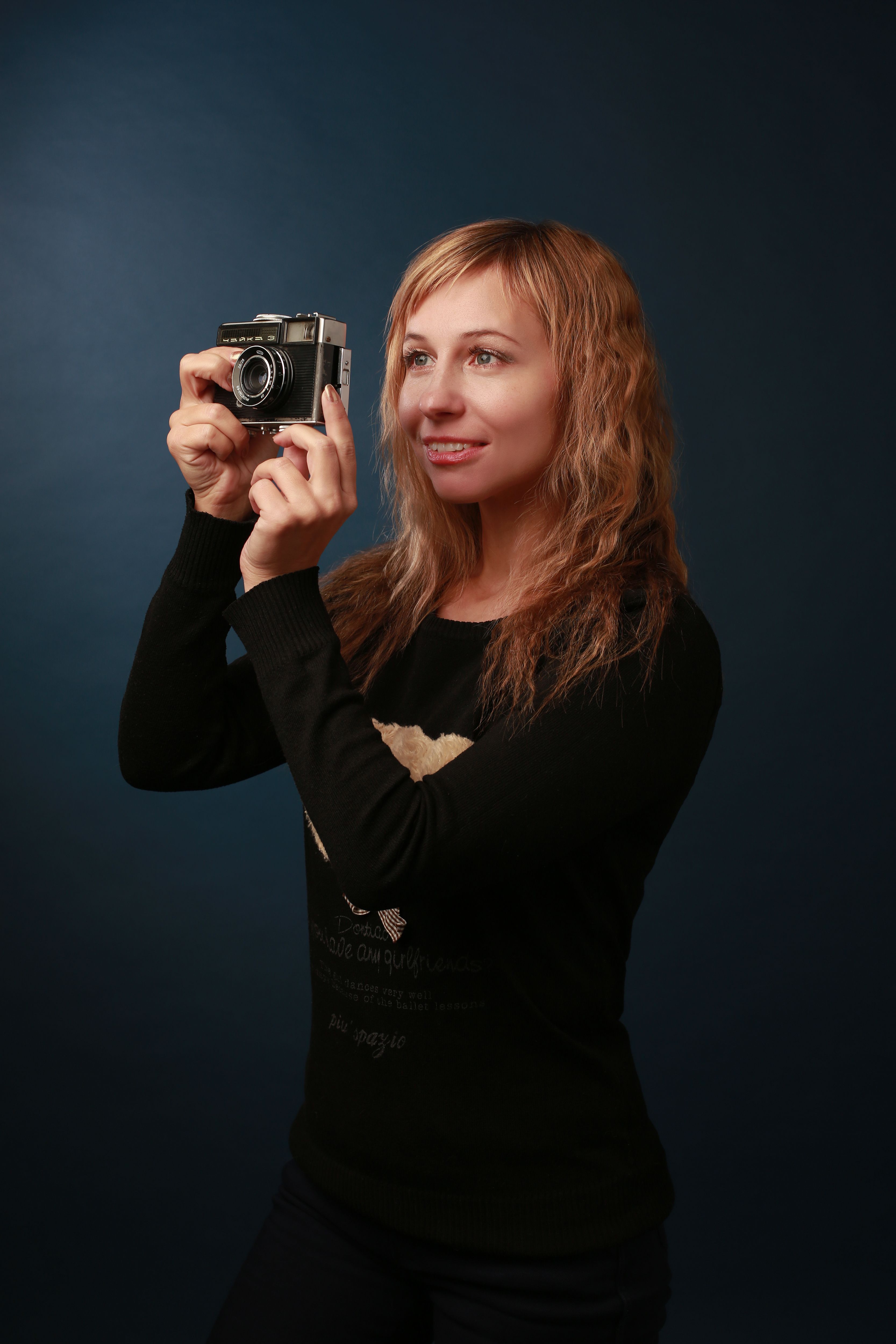 Smiling woman holding a vintage camera against a dark background.