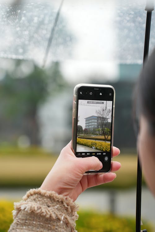 Woman under an Umbrella Taking Photo of a Building, Using a Smartphone