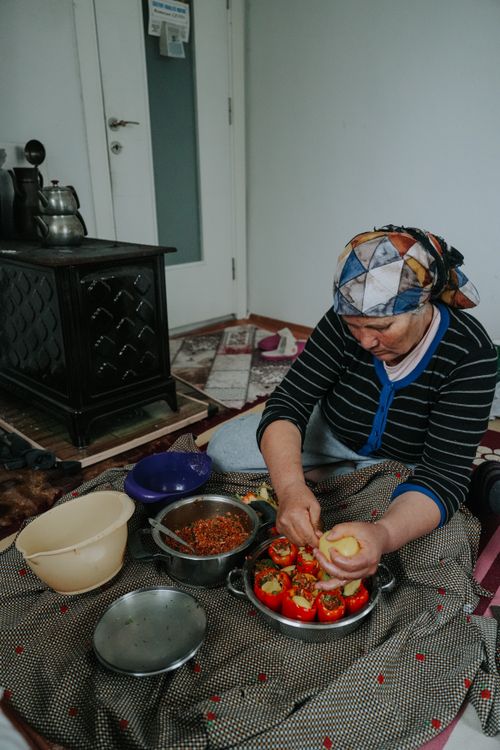 Free An elderly woman wearing a headscarf prepares stuffed peppers in a cozy indoor setting. Stock Photo