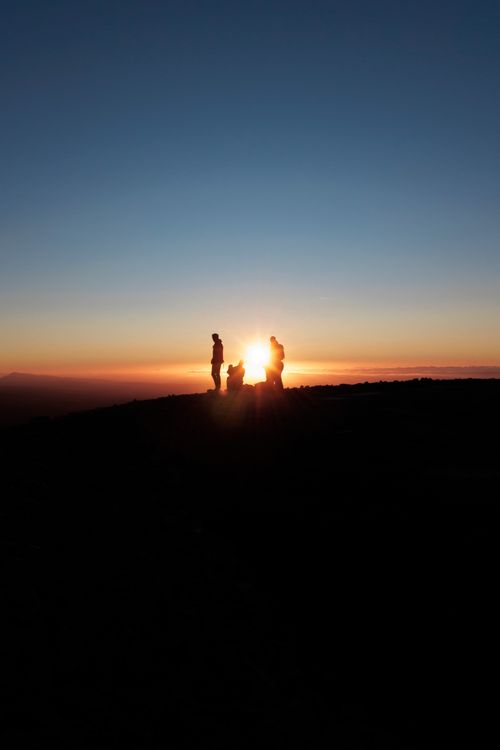 Free Silhouettes of a group standing on a hill during a vibrant sunset with clear skies. Stock Photo