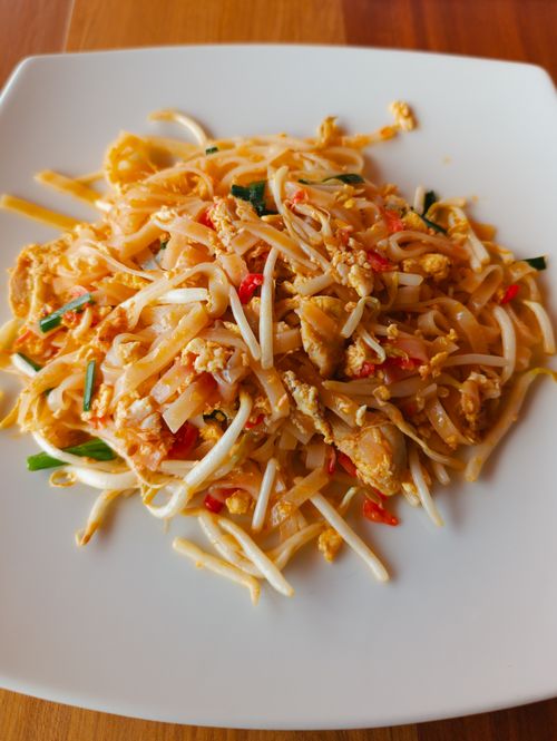 Free Mouthwatering Pad Thai noodles topped with vibrant vegetables, captured in warm natural light. Stock Photo