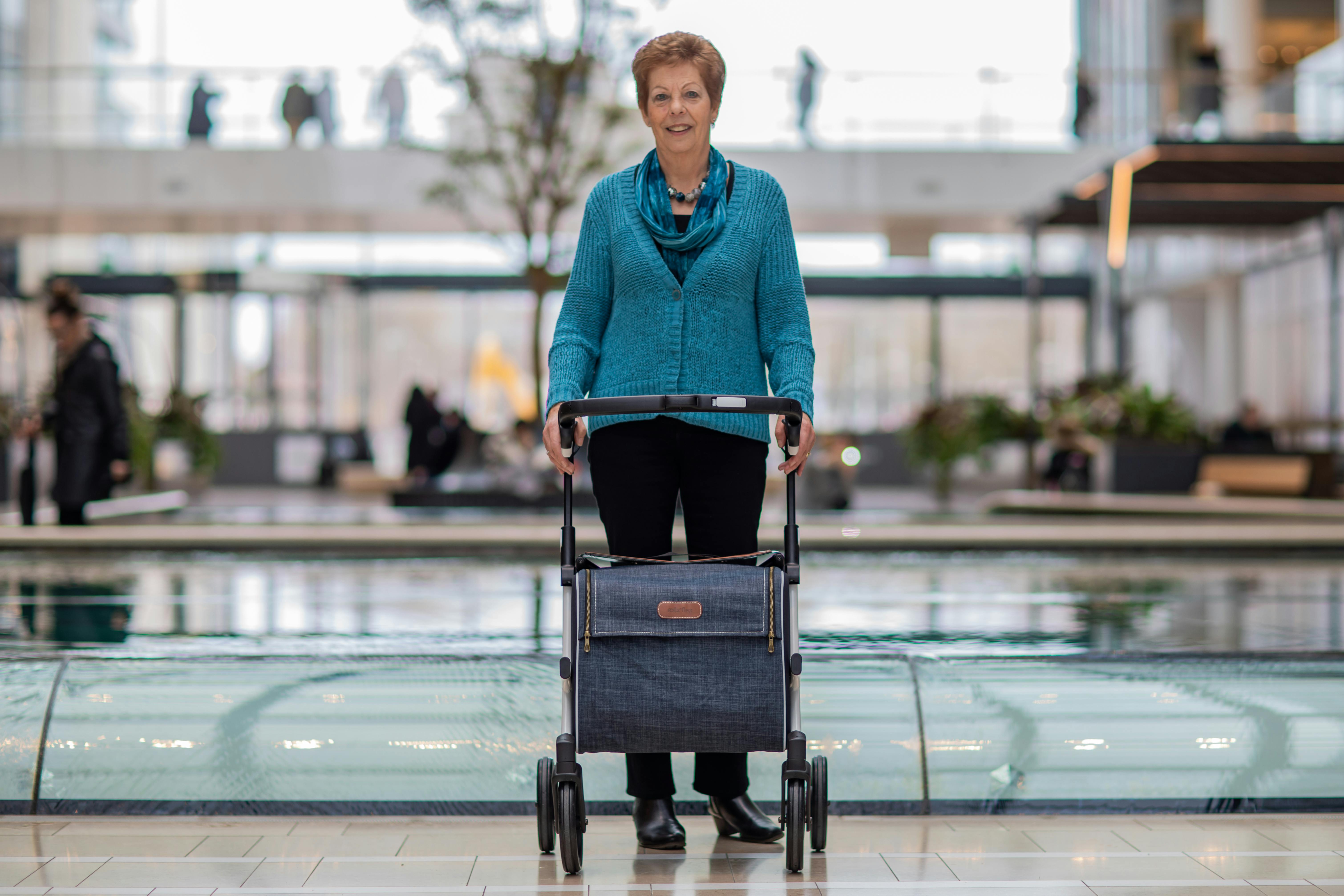 Elderly woman using a rollator walker in a stylish indoor mall environment.