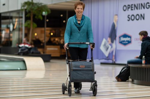 Free Elderly woman using a rollator walker in a modern shopping mall setting. Stock Photo