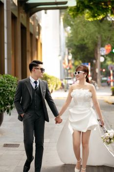 Elegant newlyweds holding hands, strolling through Hà Nội's urban setting.