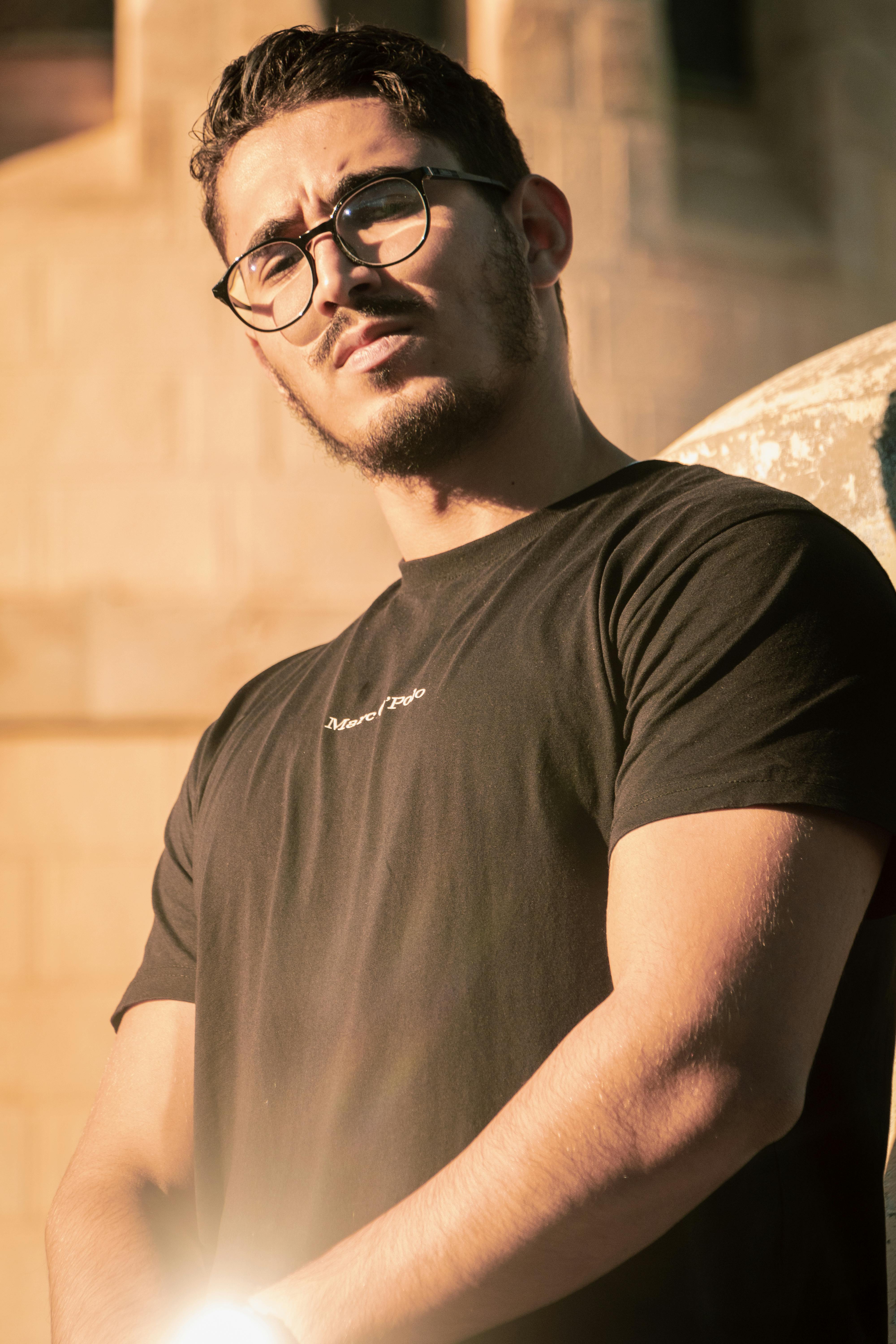 a man in glasses and a black shirt is standing in front of a stone wall