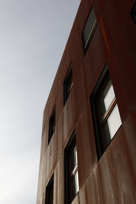 A modern building facade with a rusty metal design under a clear sky, showcasing contemporary architecture.
