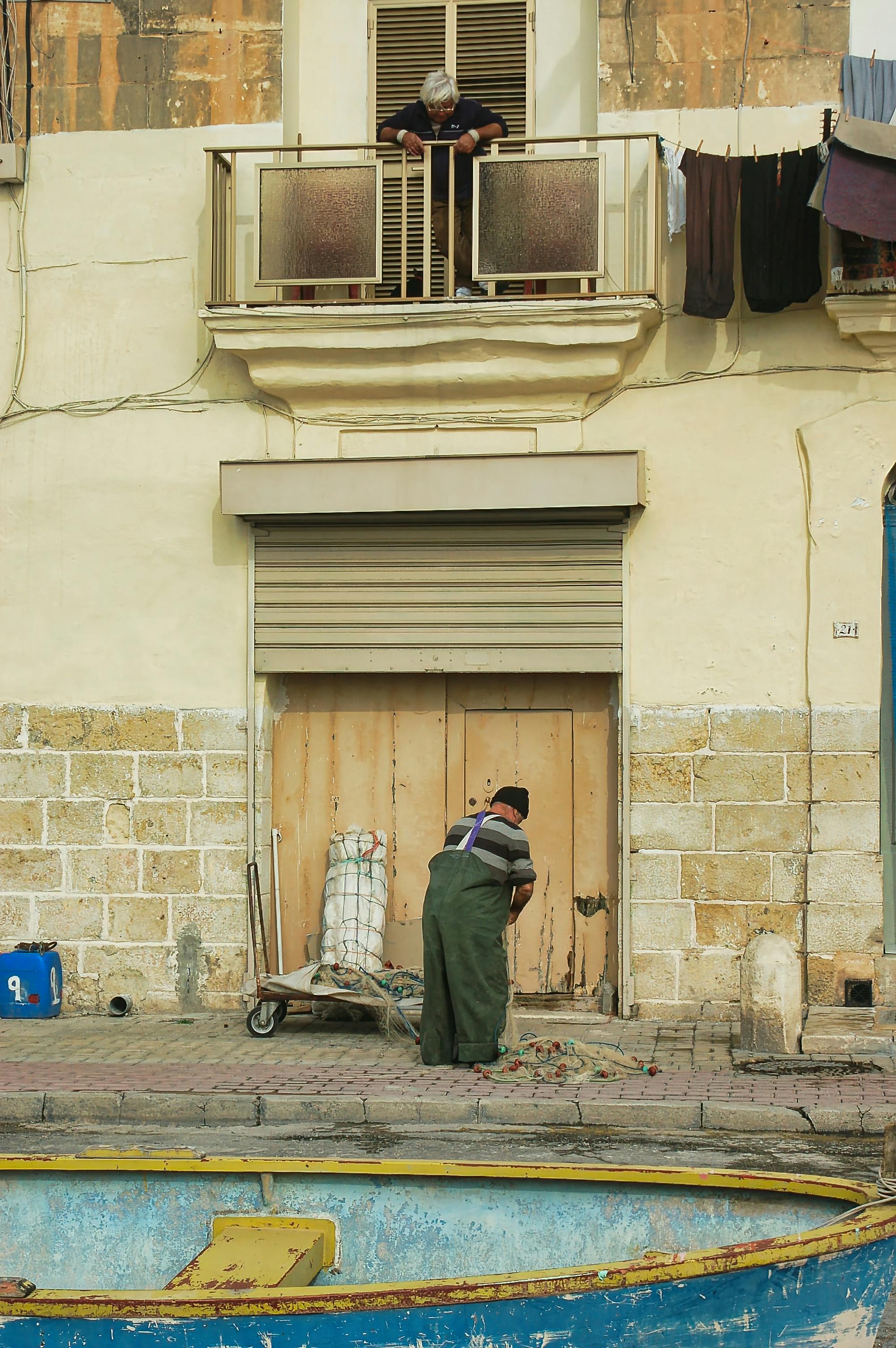 A fisherman cleans his nets by a historic building in Valletta, Malta, capturing local life.