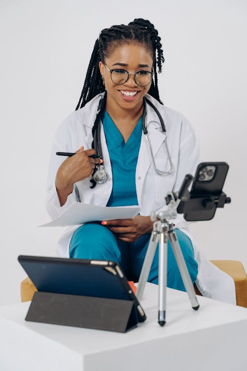 Doctor Looking at Smartphone and Taking Notes during an Online Appointment 