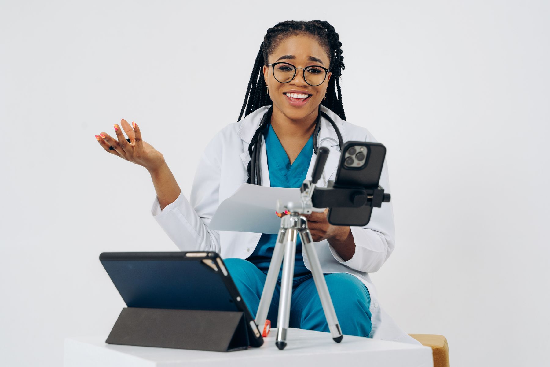 A clinician in scrubs holding a video consultation on a phone and tablet