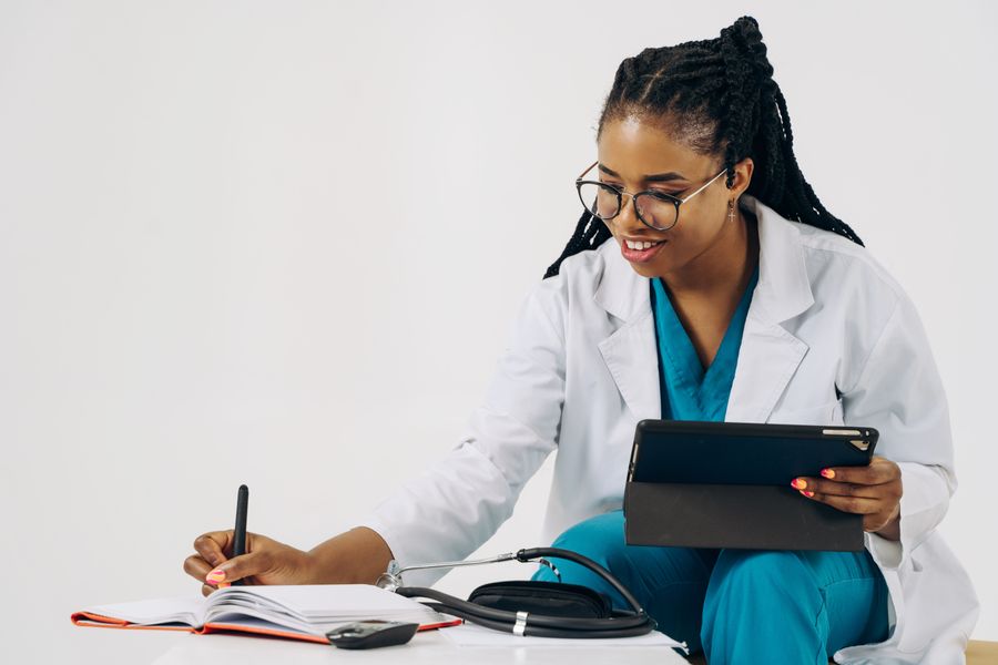Smiling female doctor in scrubs using tablet and taking notes