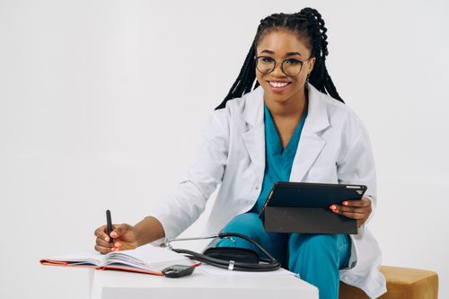 Free Smiling female doctor in scrubs with tablet and stethoscope, writing notes. Stock Photo