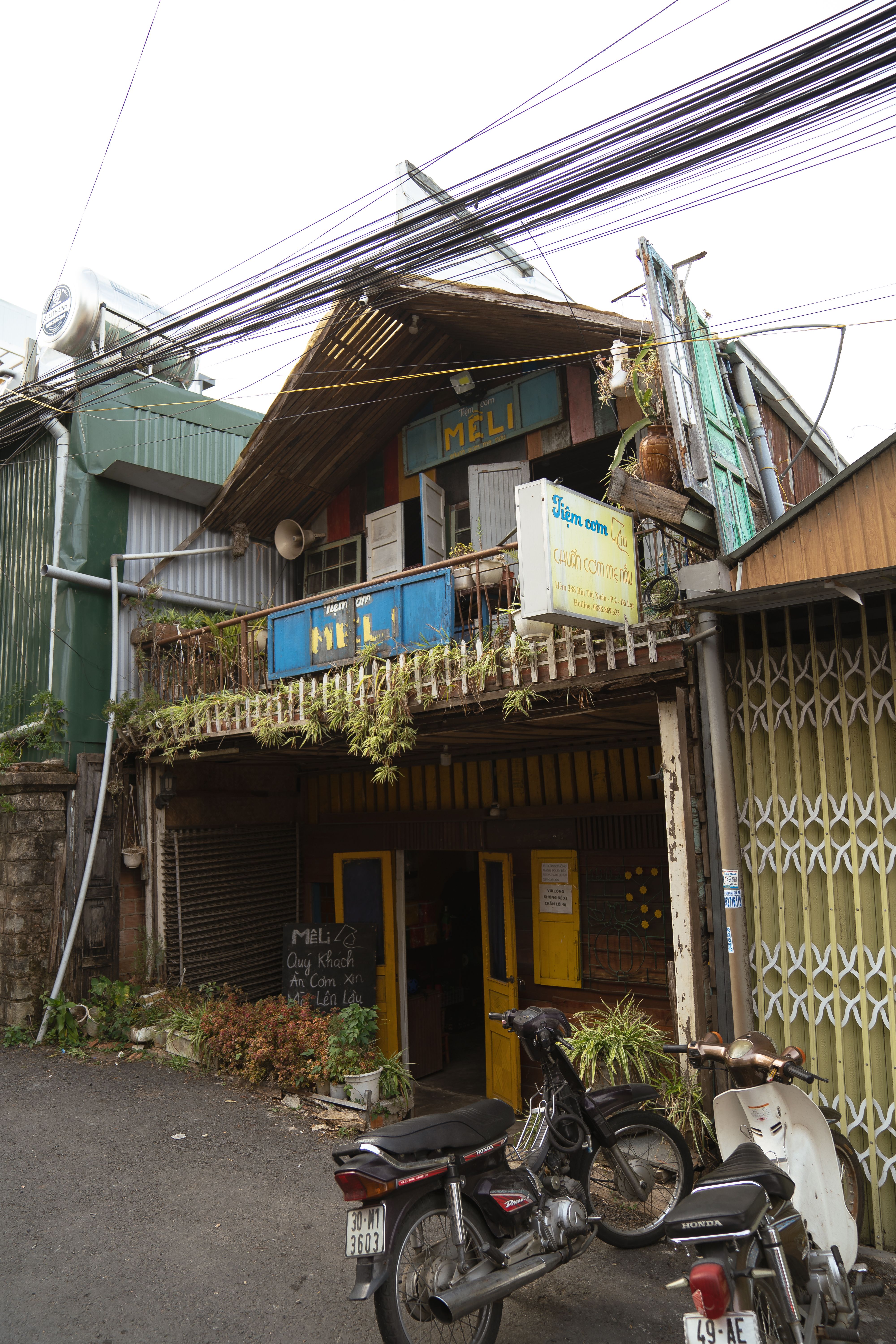Urban street view of a rustic, residential building in Vietnam with parked motorcycles.