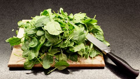 A pile of fresh spinach leaves on a wooden cutting board with a knife nearby.