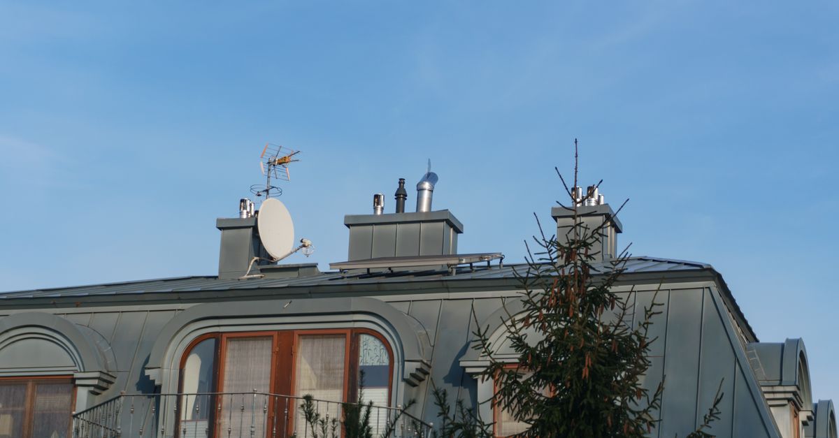 A close-up view of a building roof with antennas and a satellite dish under a clear blue sky.