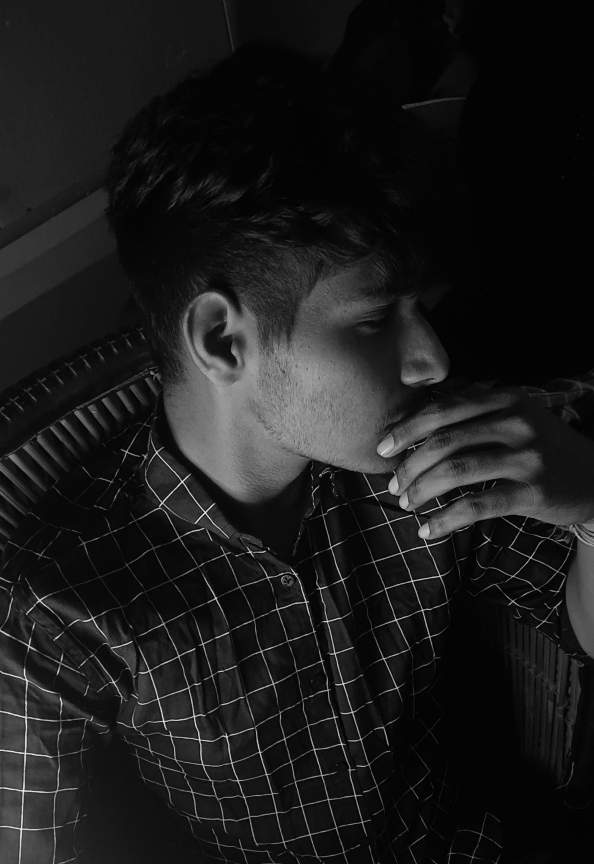 Black and white portrait of a man in a checkered shirt pondering deeply, captured in a dramatic light.