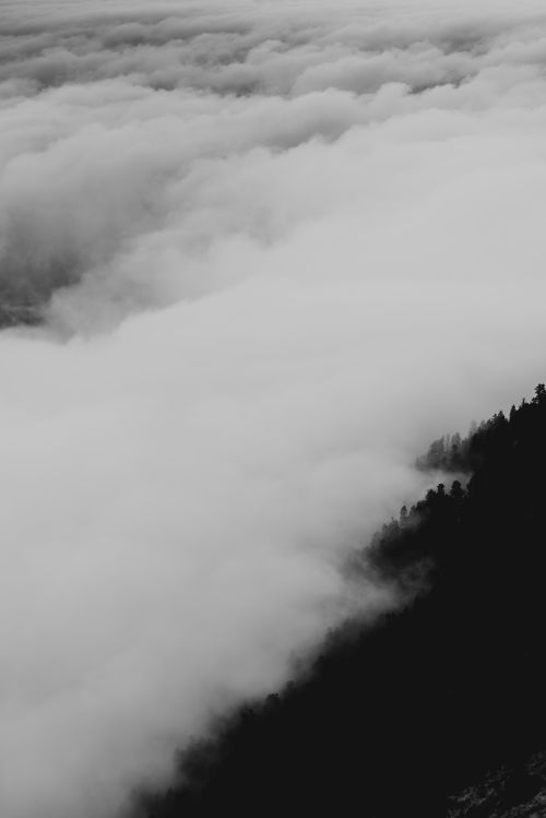 Free Aerial view of dense clouds swirling over a mountain landscape in monochrome tones. Stock Photo