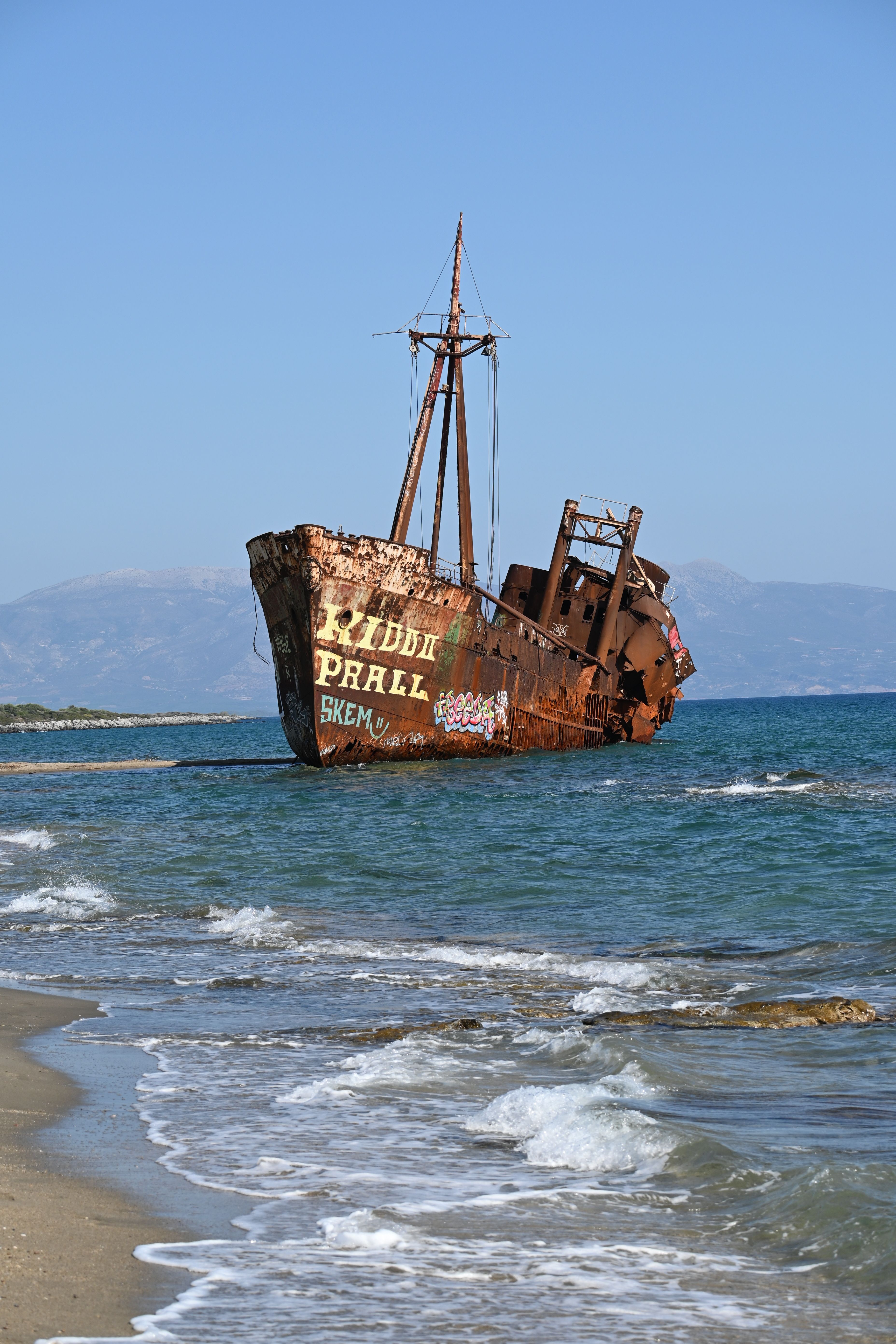 Explore the captivating sight of a rusty shipwreck along Gythio's picturesque coastline in Greece.