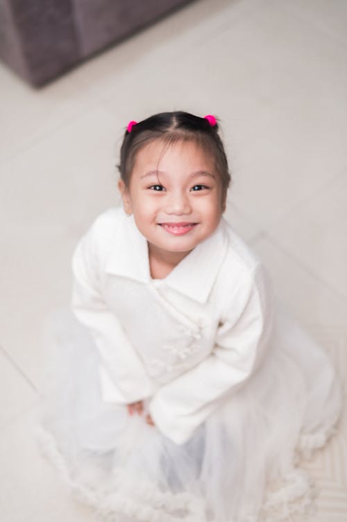 A Little Girl in a Dress Sitting on the Floor and Smiling 