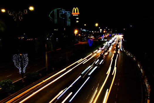 Long exposure shot capturing dynamic light trails of urban night traffic under glowing streetlights.