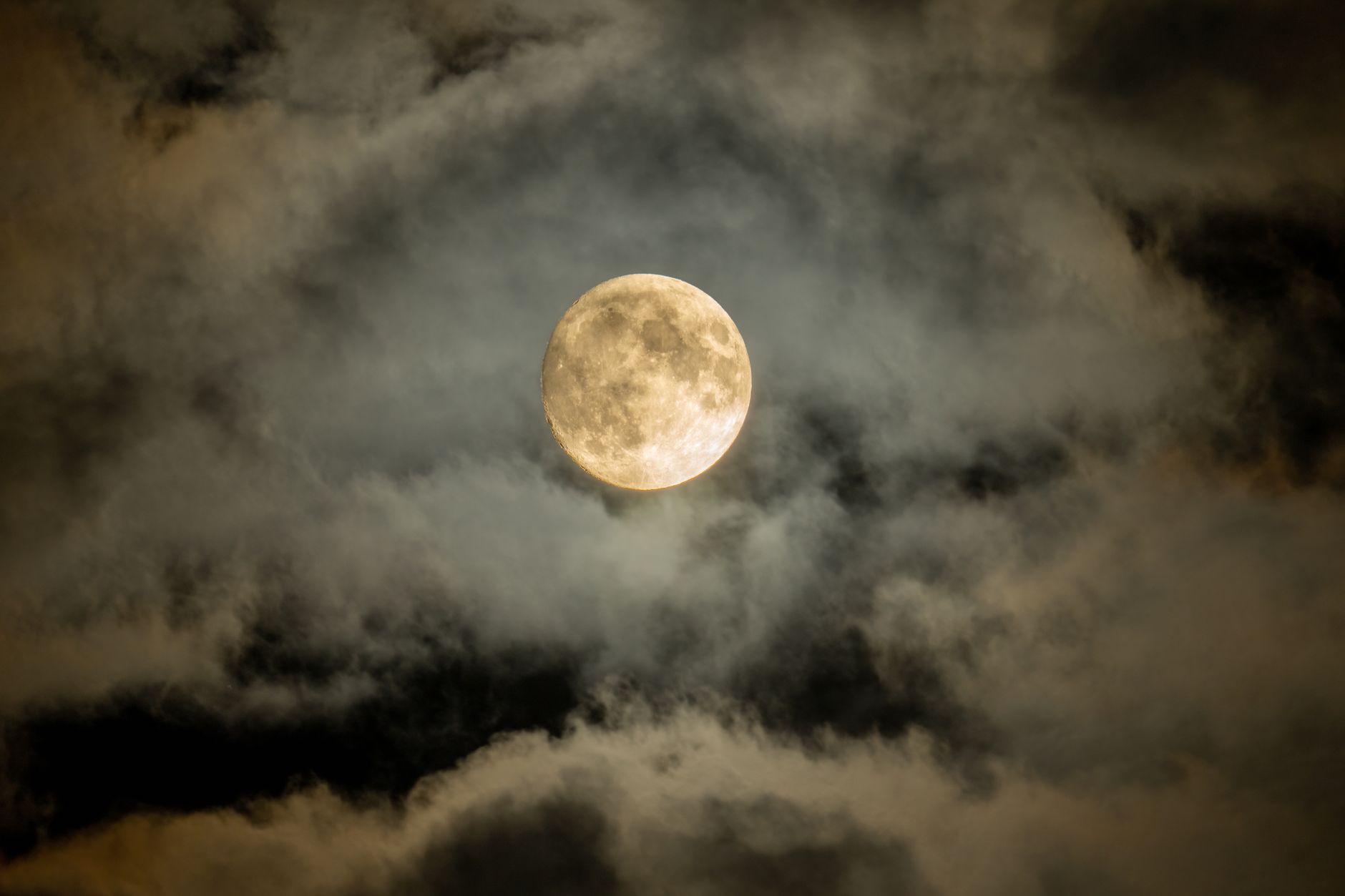 A mesmerizing full moon shining through a cloudscape in a dark, captivating night sky.