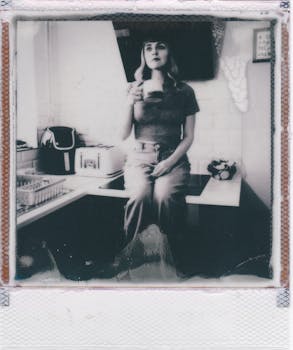 Black and white Polaroid of a woman sitting with a coffee cup in a kitchen setting.