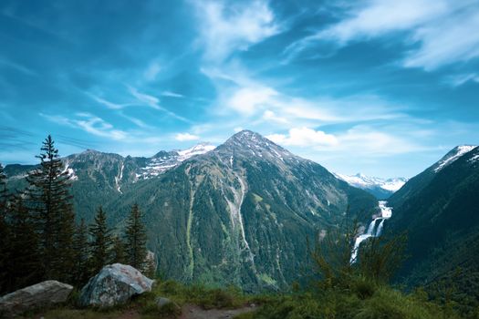 Breathtaking view of alpine mountains with a cascading waterfall under a vibrant blue sky.
