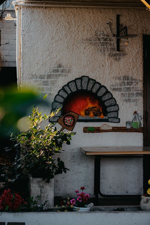 Free Charming wall art depicting a traditional wood-fired oven with plants and a table. Stock Photo