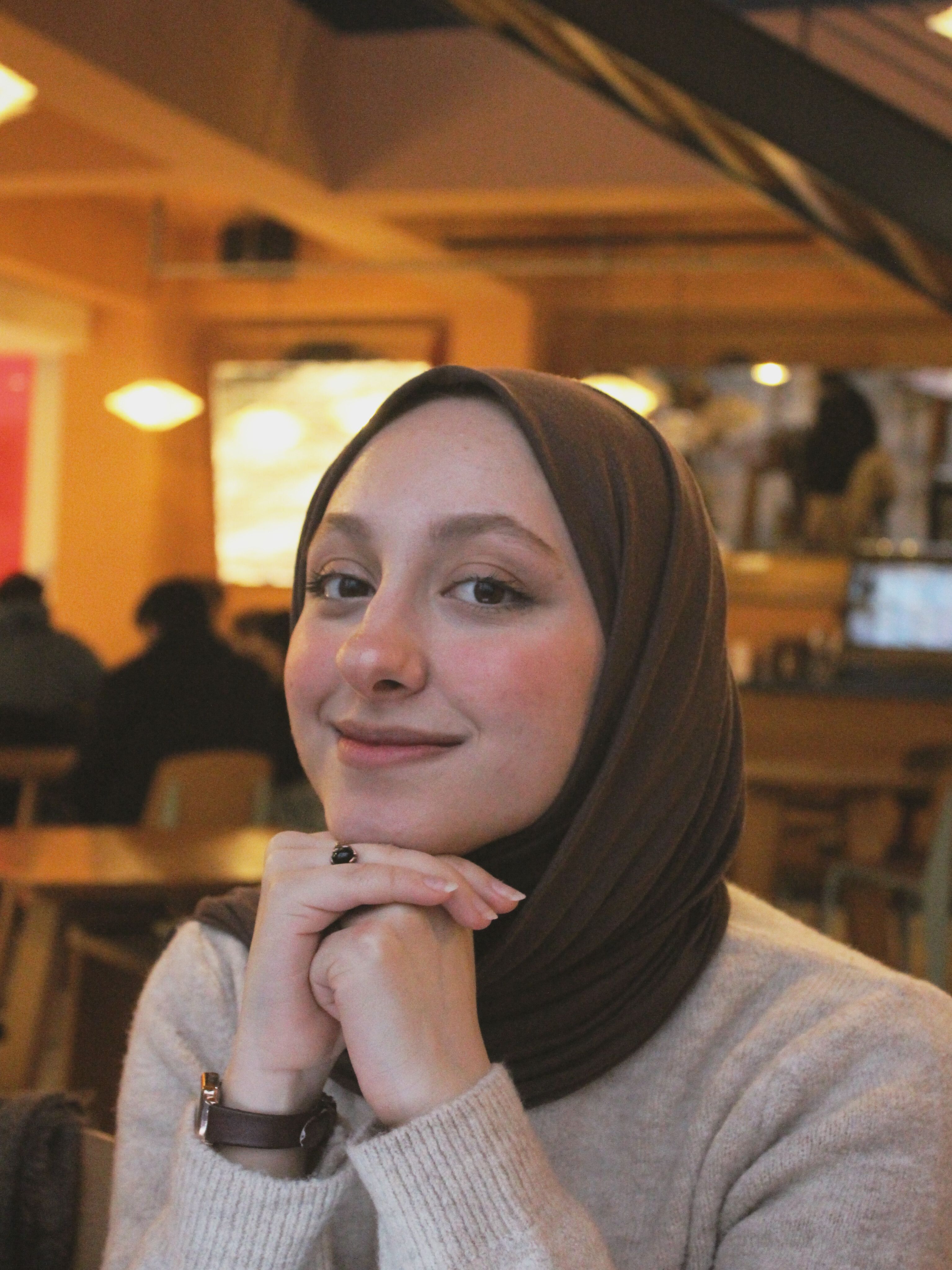A woman in a headscarf smiles warmly while sitting in a cozy café, creating an inviting atmosphere.