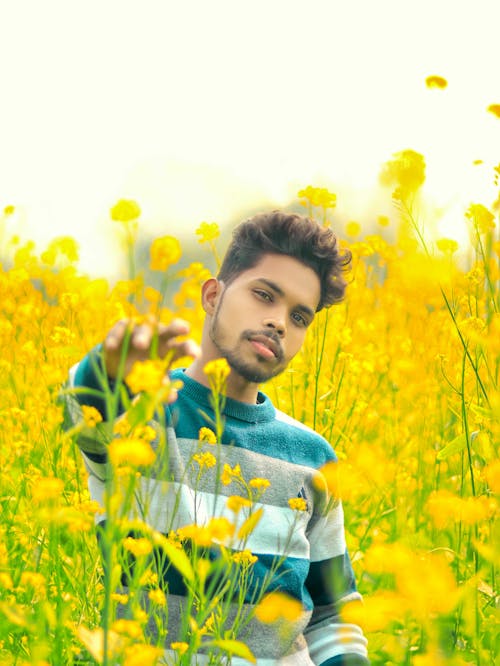 Young Man Standing between Yellow Flowers on a Field 