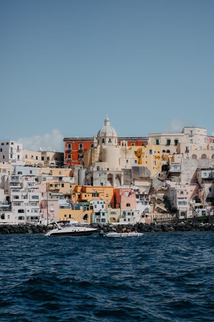 Vibrant waterfront houses in Procida, Italy with blue sky and sea.