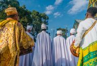 Men in traditional Ethiopian attire participating in a religious ceremony outdoors, under a clear blue sky.