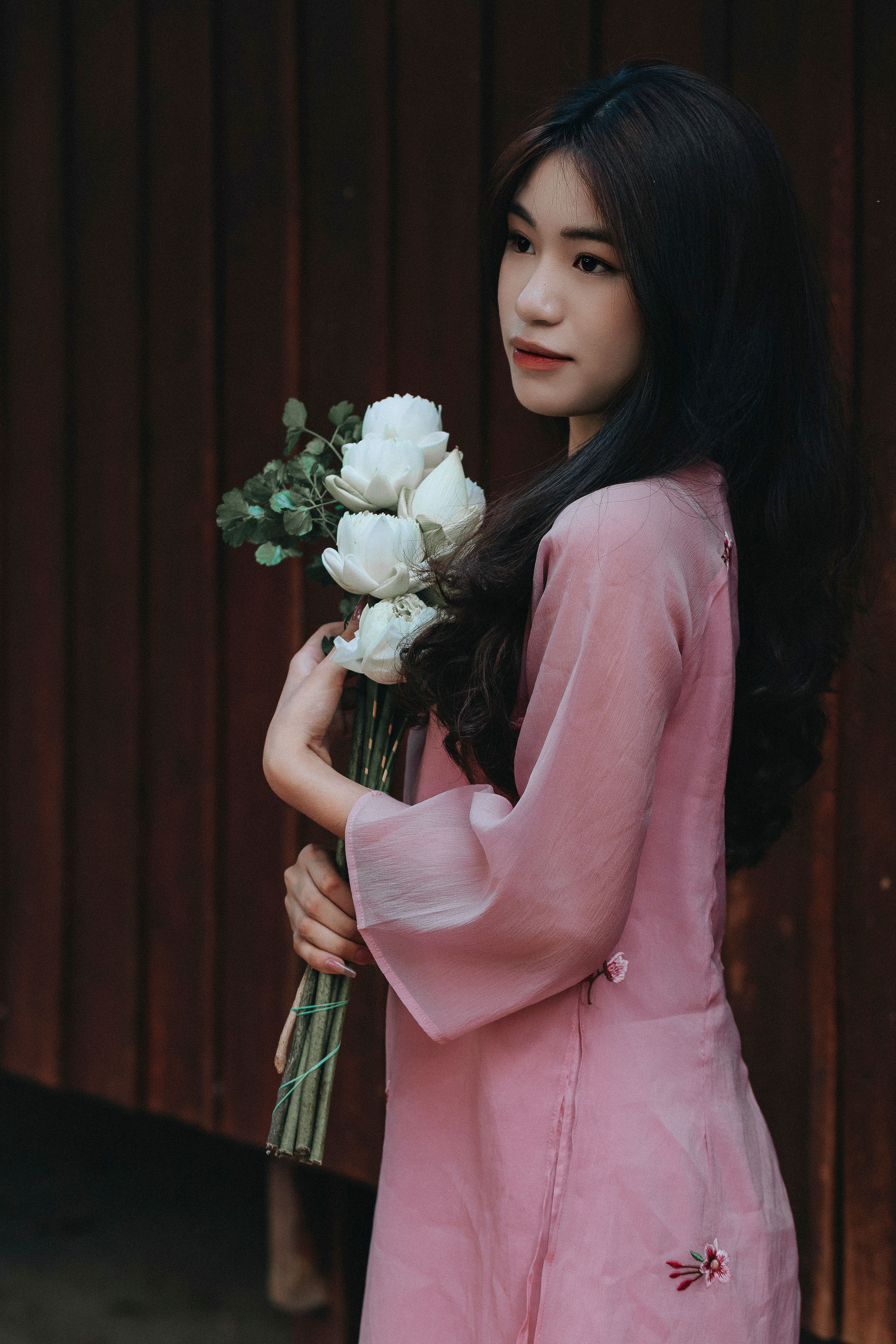 Elegant Vietnamese woman in traditional pink ao dai holding a bouquet of white flowers.
