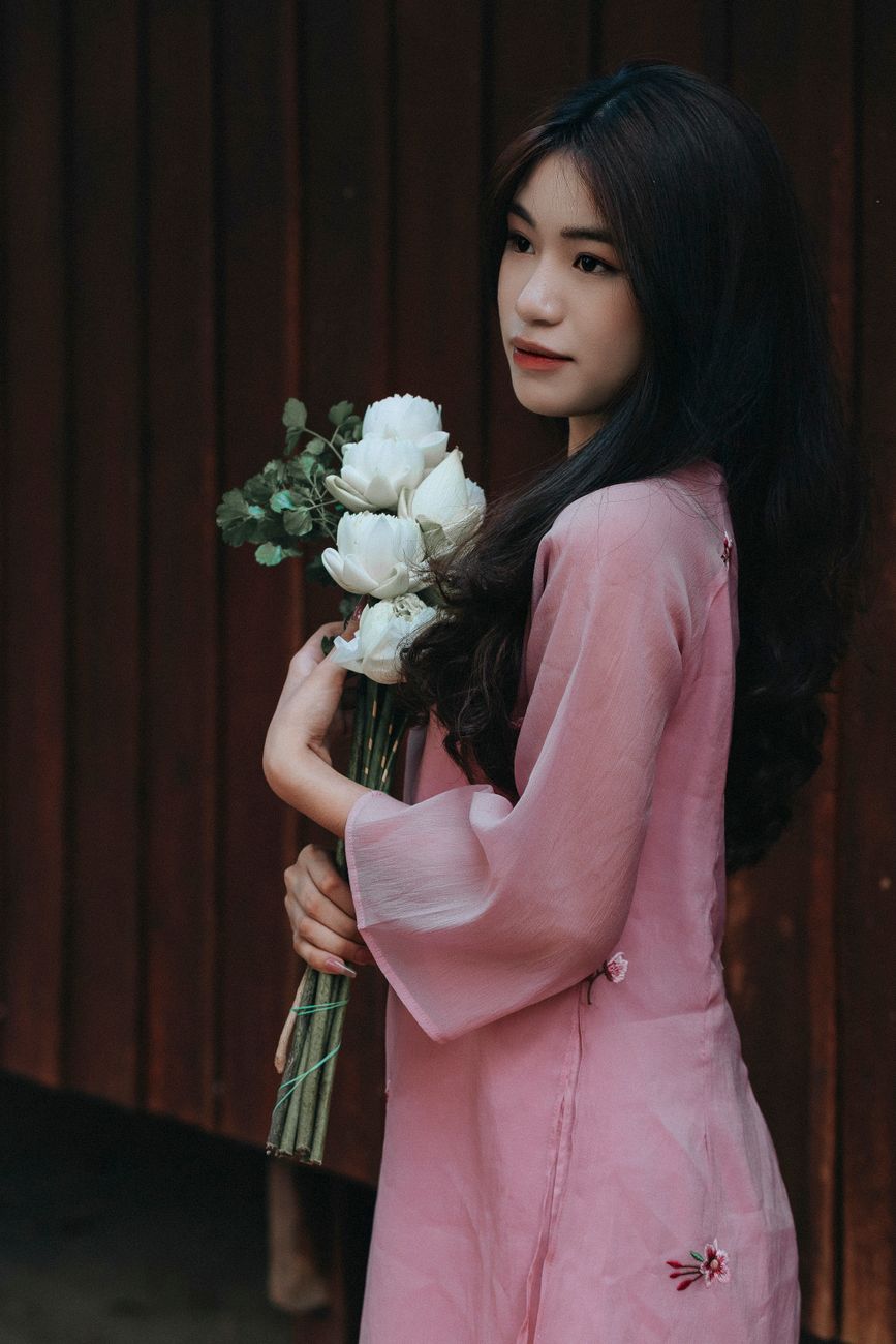 Elegant Vietnamese woman in traditional pink ao dai holding a bouquet of white flowers.