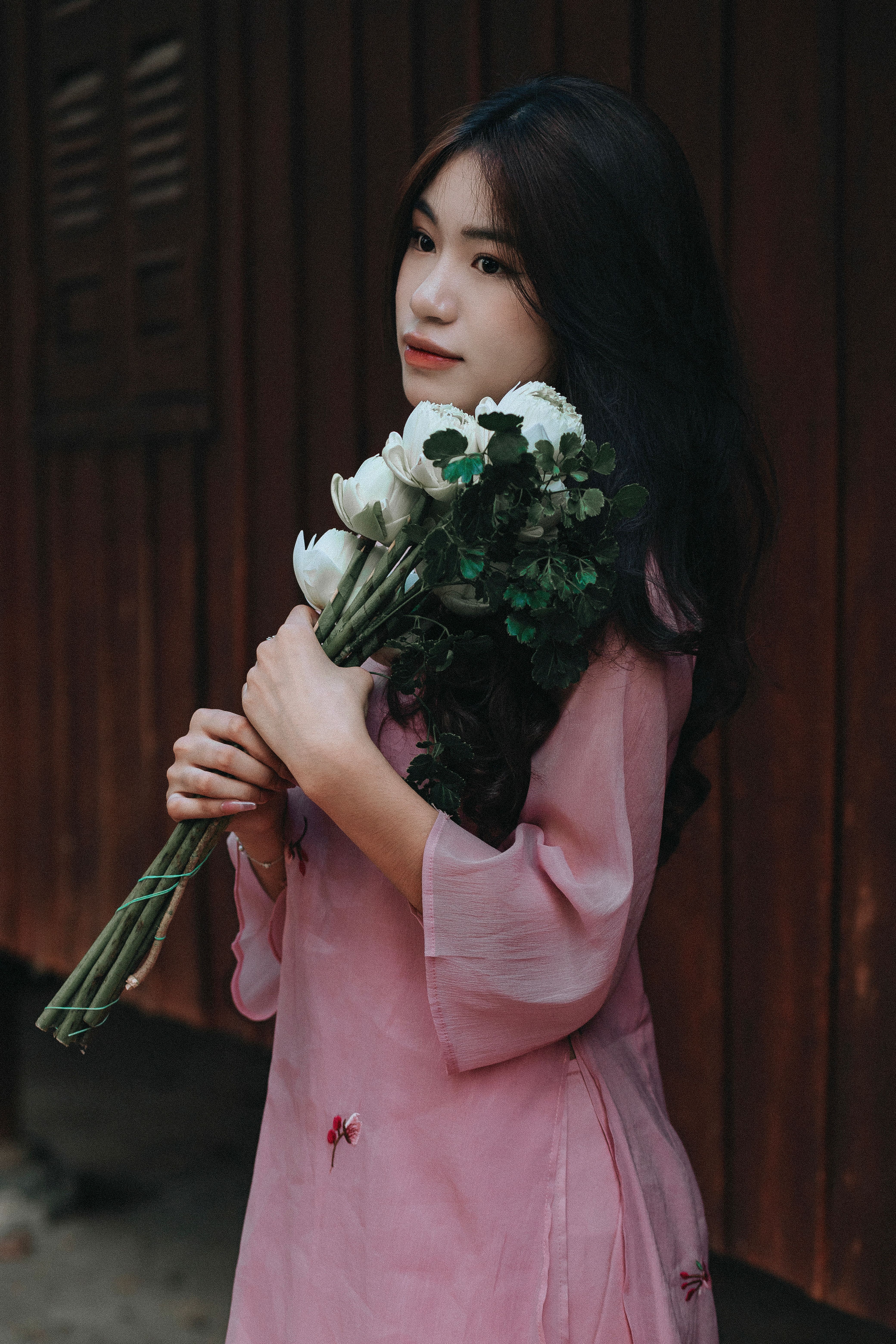 Beautiful woman in pink dress holding a bouquet of white flowers, standing outdoors.