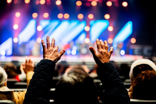 Back View of an Elderly Person Standing at a Concert with Raised Arms 