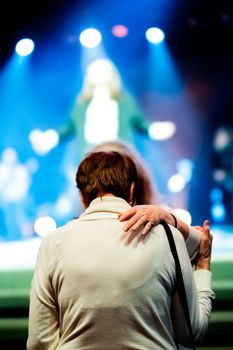 A couple in an embrace at a vibrant live concert with colorful stage lighting.