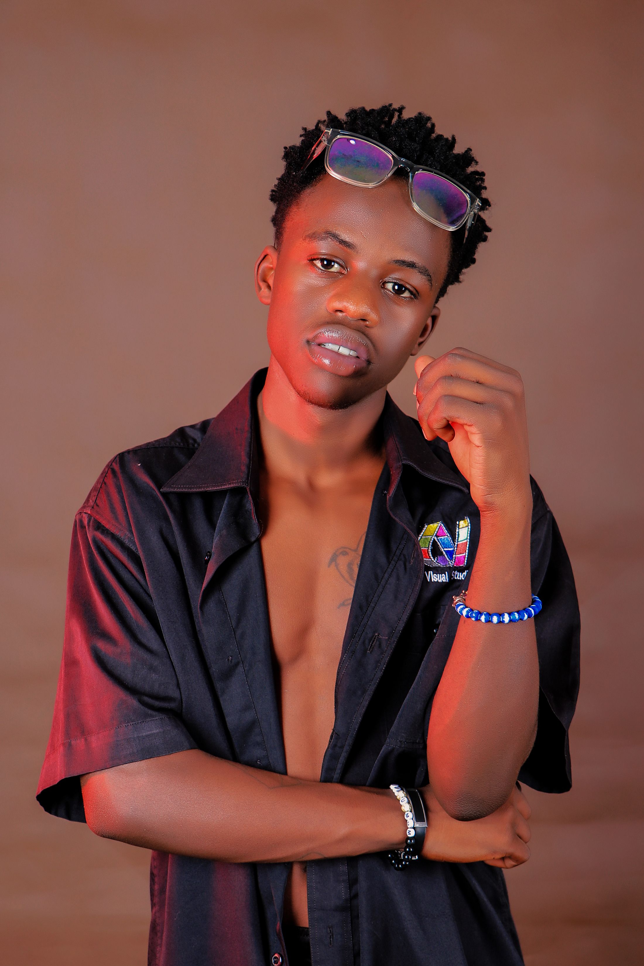 A young man striking a pose in a trendy unbuttoned shirt, wearing sunglasses indoors.