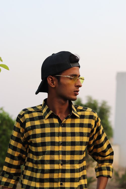 Free Portrait of a young man in a checkered shirt and cap looking to the side outdoors. Stock Photo
