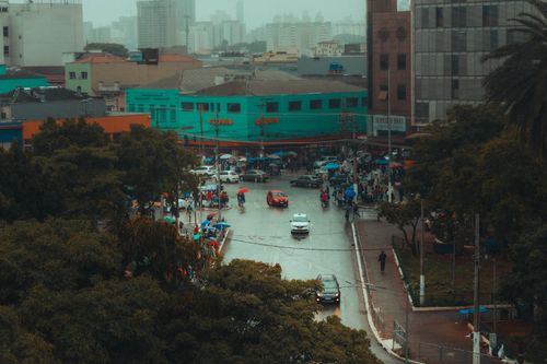 Free Aerial view of a bustling city intersection on a rainy day, with people and vehicles navigating the wet streets. Stock Photo