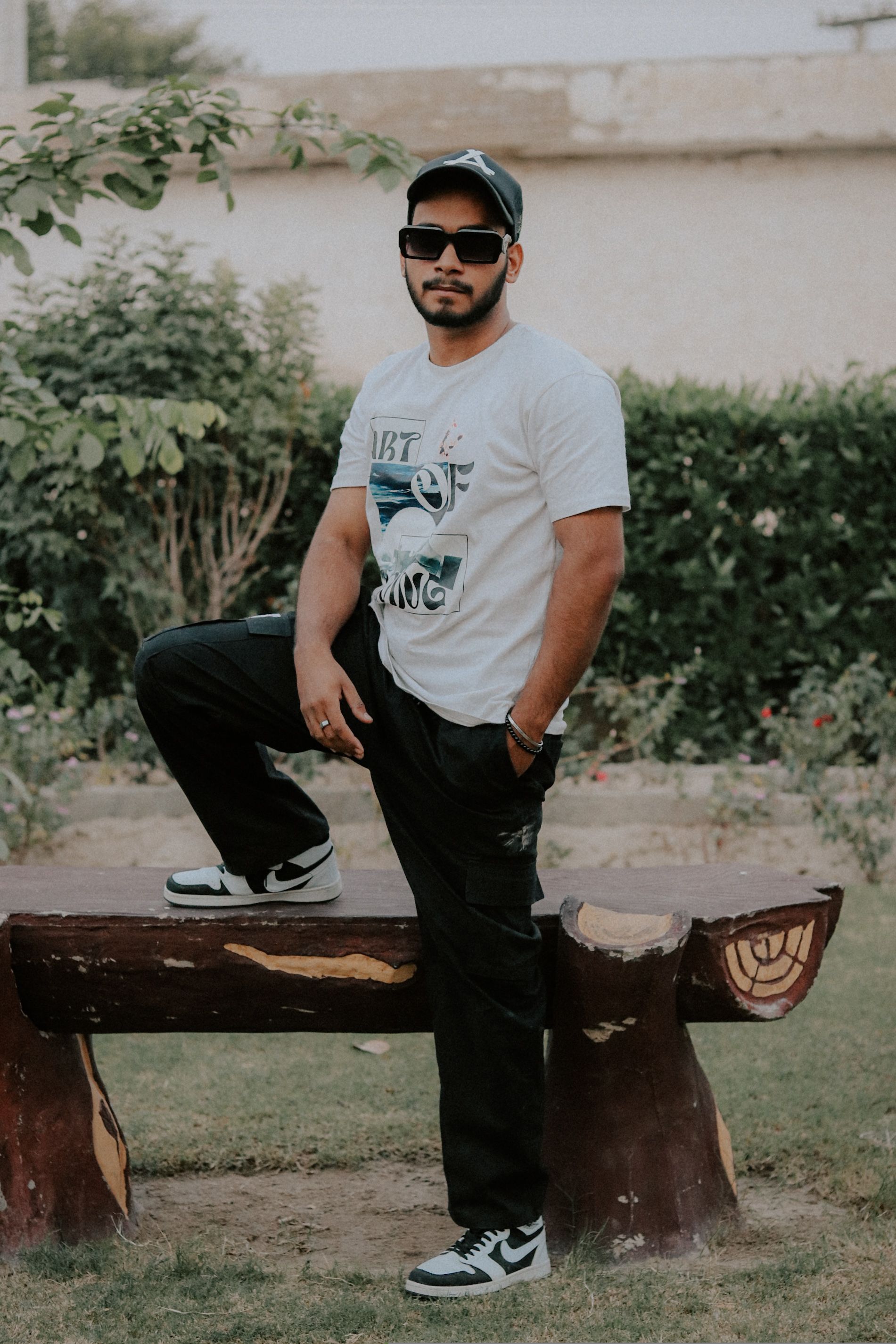 A young man in casual attire, posing confidently outdoors on a bench.